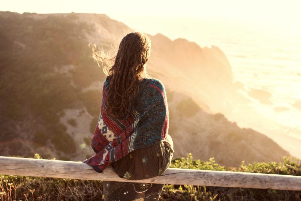 A traveler sitting above the coast watching the sunset